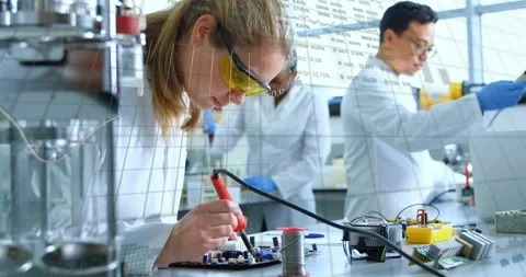 Lab tech soldering PCB while teammate tuning meter causing data overlay for Stock Footage 330621533