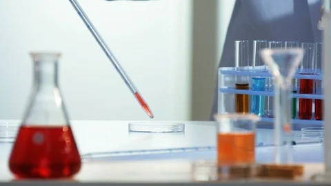 Lab technician adds a few drops of a red chemical from a pipette to a petri dish Stock Footage 88379007