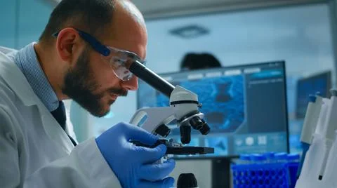 Lab technician examining samples and liquid using microscope Foto stock