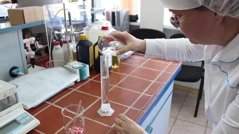 A lab technician in the laboratory pours liquid from a flask into a test tube. Stock Footage 128374571