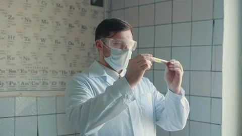 Lab technician in a protective suit and glasses holds a test tube in his hands Stock Footage 131370255