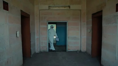 Lab technician in a protective suit and goggles comes out of the door and begins Stock Footage 131375875