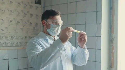 Lab technician in a protective suit and glasses holds a test tube in his hands Stock Footage 133077880