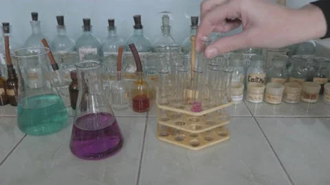 Lab technician puts a test tube in a support under laboratory flasks. Stock Footage 86069348