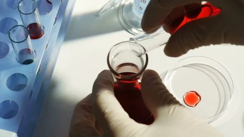 Lab worker pours chemicals from a test tube into a flask Stock Footage 88380472