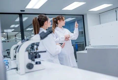 Lab workers discuss findings while using lab equipment in a modern facility.. Fotos Stock