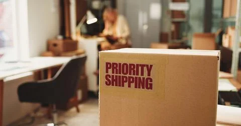 Label, priority shipping and box in office for distribution with logistics .. Stock Photos