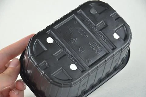Labeled black plastic PP5 container in a hadn upside down on a white background Stock-Fotos