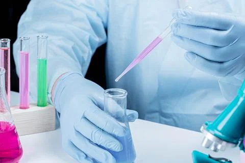 Laboratory assistant in gloves with a flask and pipette working at the table Stock Photos