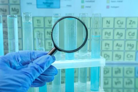 Laboratory assistant looking through magnifying glass on test tubes against.. Stock Photos