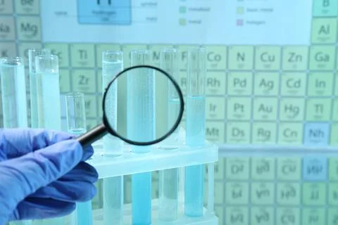 Laboratory assistant looking through magnifying glass on test tubes against.. 写真素材
