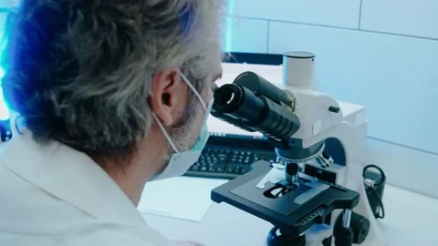 Laboratory assistant looks through a microscope in white bright lab Stock Footage 166664545