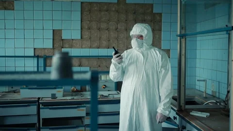 The laboratory assistant in a protective suit and glasses holds a walkie-talkie Stock Footage 133000185