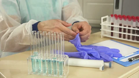 Laboratory assistant sitting at the desk puts on protective latex gloves. Ready Stock Footage 129751305
