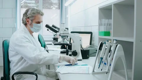 Laboratory assistant works with a microscope and writes notes at white lab Video stock 166664500
