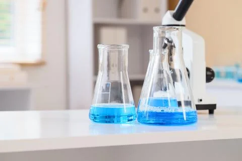 Laboratory flasks with blue liquid and microscope Stock Photos