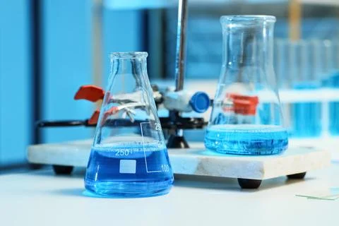 Laboratory flasks with blue liquid on white table, scientific research and ch Stock Photos