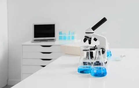 Laboratory microscope with blue liquid in flasks on white table Stock Photos