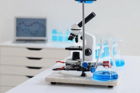 Laboratory setup with blue liquid in an erlenmeyer flask, microscope, and lap Stock Photos