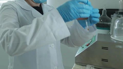 A laboratory technician in a white coat and protective gloves pours liquid into Stock Footage 264864835