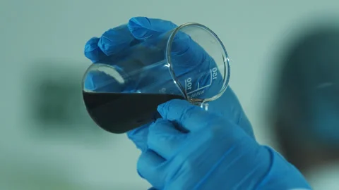 A laboratory technician in a white coat and protective gloves pours liquid into Stock Footage 264864841