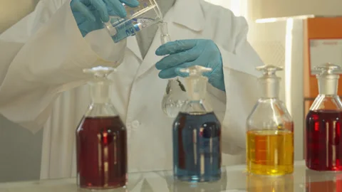 A laboratory technician in a white coat and protective gloves pours liquid into Stock Footage 311503399