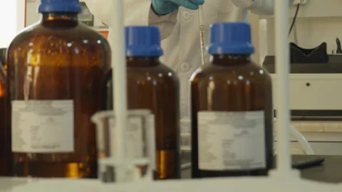 A laboratory technician in a white coat and protective gloves pours liquid into Stock Footage 333461266