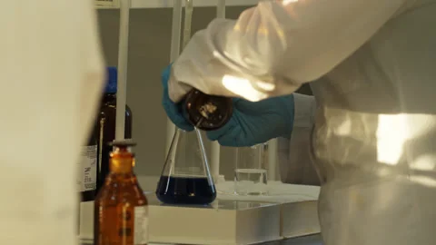 A laboratory technician in a white coat and protective gloves pours liquid into Stock Footage 333461597