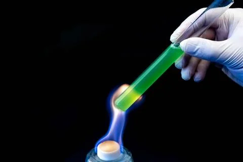 A laboratory test tube with a green solution in a man's hand is heated over.. Fotos de archivo