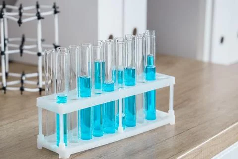 Laboratory test tubes with blue liquid in a white rack on a wooden table, sci Stock Photos