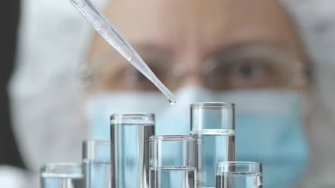 Laboratory testing. Scientist or assistant in protective mask adds liquid from Stock Footage