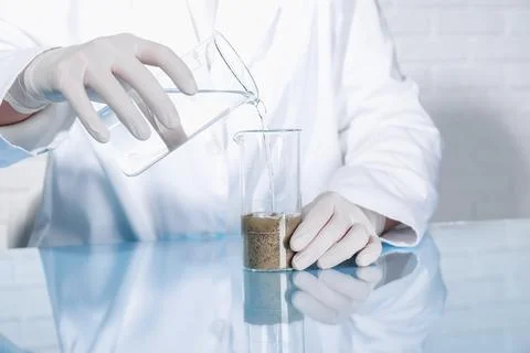 Laboratory testing. Scientist pouring liquid into beaker with soil sample a.. Foto stock