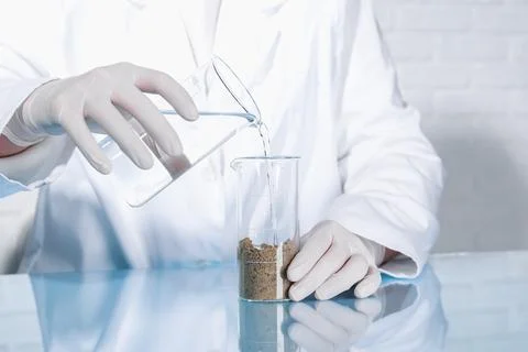 Laboratory testing. Scientist pouring liquid into beaker with soil sample a.. Foto stock
