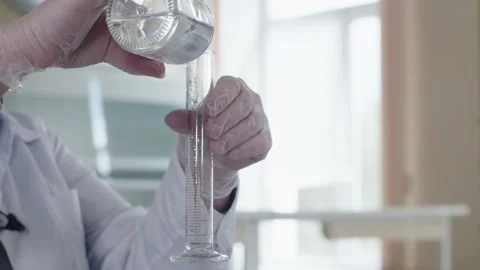 Laboratory worker is holding two glass flasks in hands and pouring liquid Stock Footage 201344791