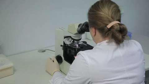 Laboratory worker sits at a microscope. in medical uniform Video stock 132251572