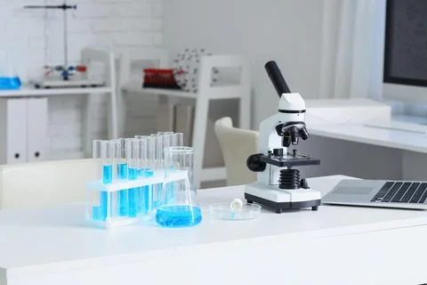 Laboratory workspace with microscope and blue liquid test tubes Stock Photos