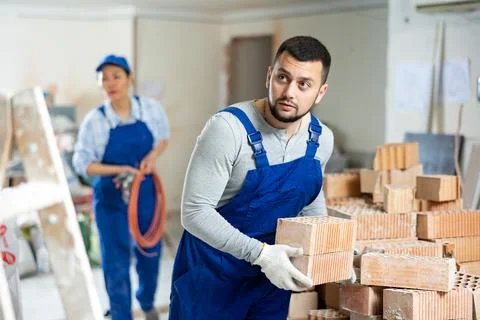 Laborer in blue overalls stacking bricks at construction site indoors 写真素材