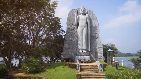 Laborer Cutting Grass in front of Buddha Statue. Minneriya Temple. Sri Lanka Vidéo 85409316