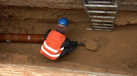Laborer laying water main in a deep, unprotected trench. Stock Footage 62687764