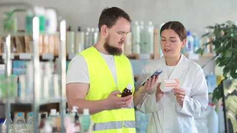 Laborer man builder in pharmacy scans QR code on expectorant syrup, pharmacist Stock Footage 309548713