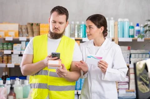 Laborer man builder in pharmacy scans QR code on pills box, pharmacist offer Foto stock