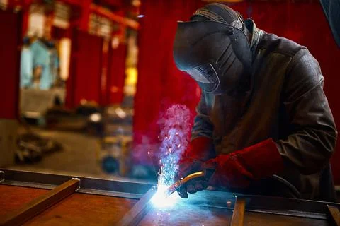 Laborer in protective mask welds manually metal frame Stock Photos