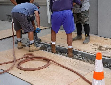 Laborer workmen are seen digging a trench through a concrete driveway to re.. Stock Photos