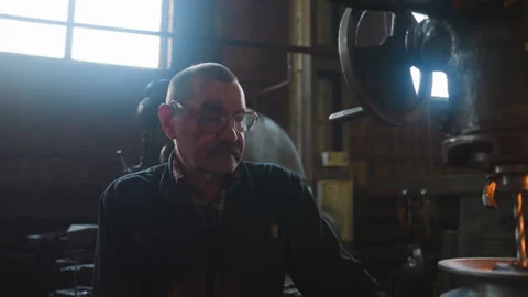 Labourer with spectacles sits by drilling machine at factory 스톡 동영상 243306789