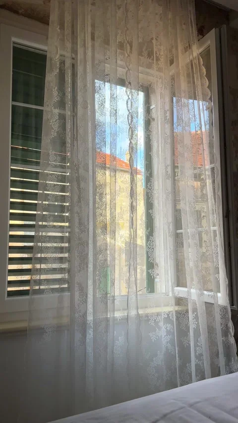 Lace curtains hanging on an open window with a view of old European stone Stock Footage 341664038