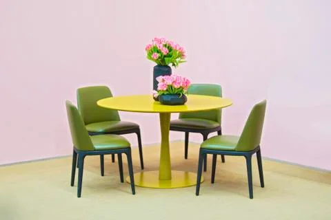 Laconic interior of the dining room. Yellow round table and green leather cha Stock Photos