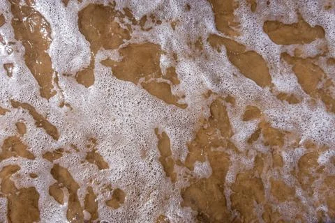 Lacy pattern of wave and sea foam rolling onto the shore Stock Photos