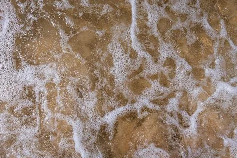 Lacy pattern of wave and sea foam rolling onto the shore Stock Photos