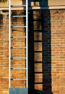 Ladder casting shadow on a worn old stained brick wall Stock Photos