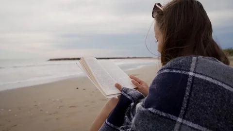 LADISPOLI, ITALY - MAY 13, 2019: Girl turns book pages while reading on seashore 库存影片 123550853